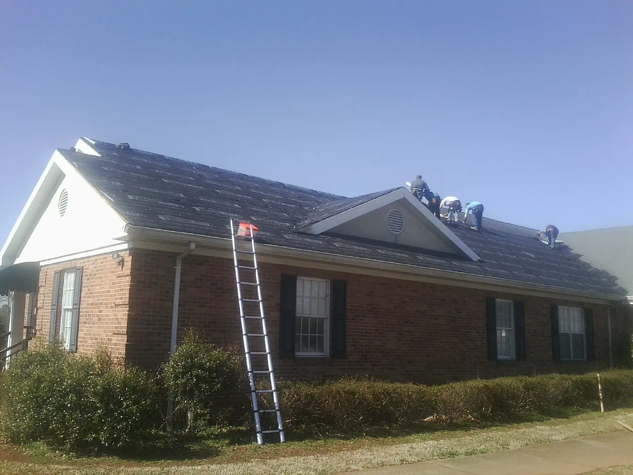 Crew tearing shingles off a brick ranch roof with a ladder set — Metal Roof Repair work by our crew in Mukwonago