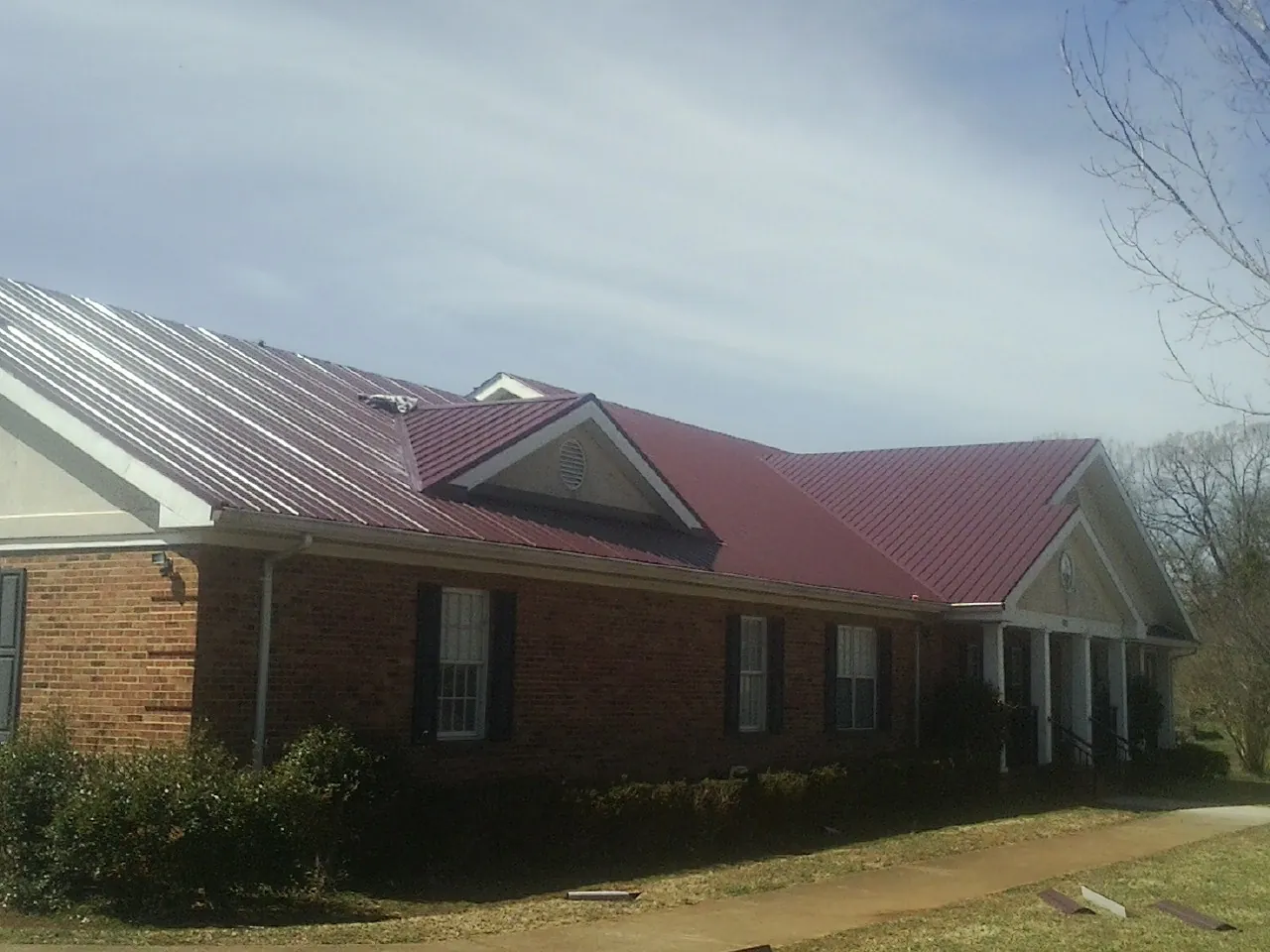 Red metal roof with gabled entries on a long brick building, from a Hail Damage Roof Repair job in Mukwonago