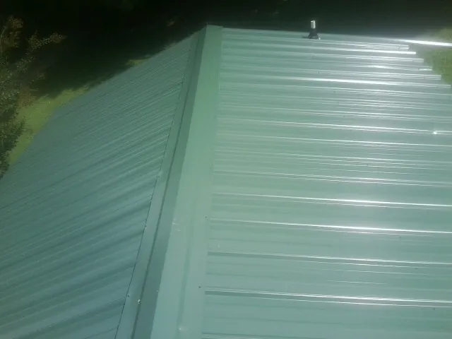 New green metal panels meeting at the ridge of a roof — Flat Roof Repair work by our crew in Mukwonago